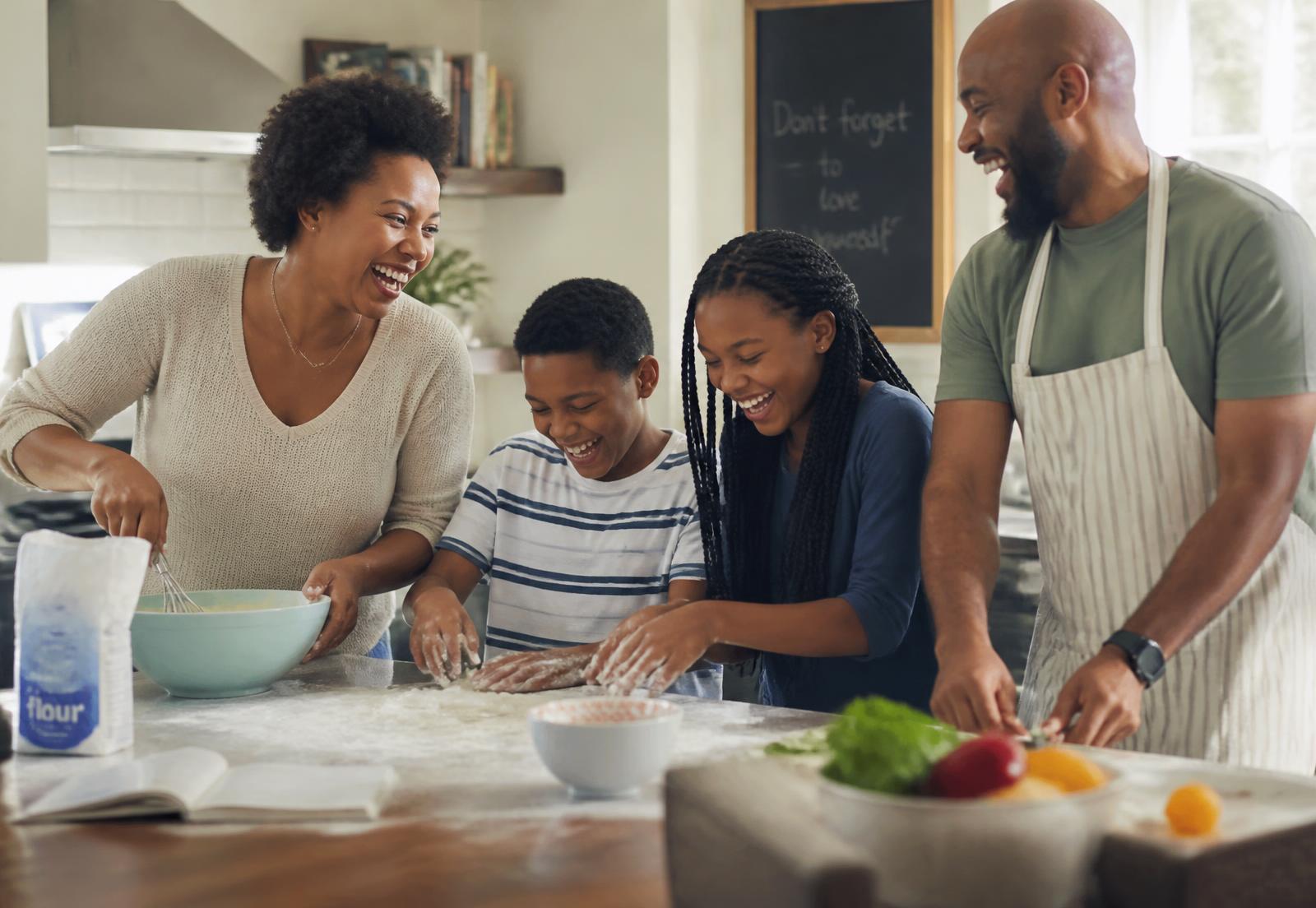 A family of four laughing while baking together in a bright, lived-in kitchen.